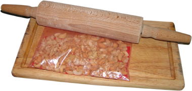 orzechy nerkowca praone z dodatkiem soli, drewniana deska do krojenia, woreczek foliowy, drewniany waek do wakowania ciasta